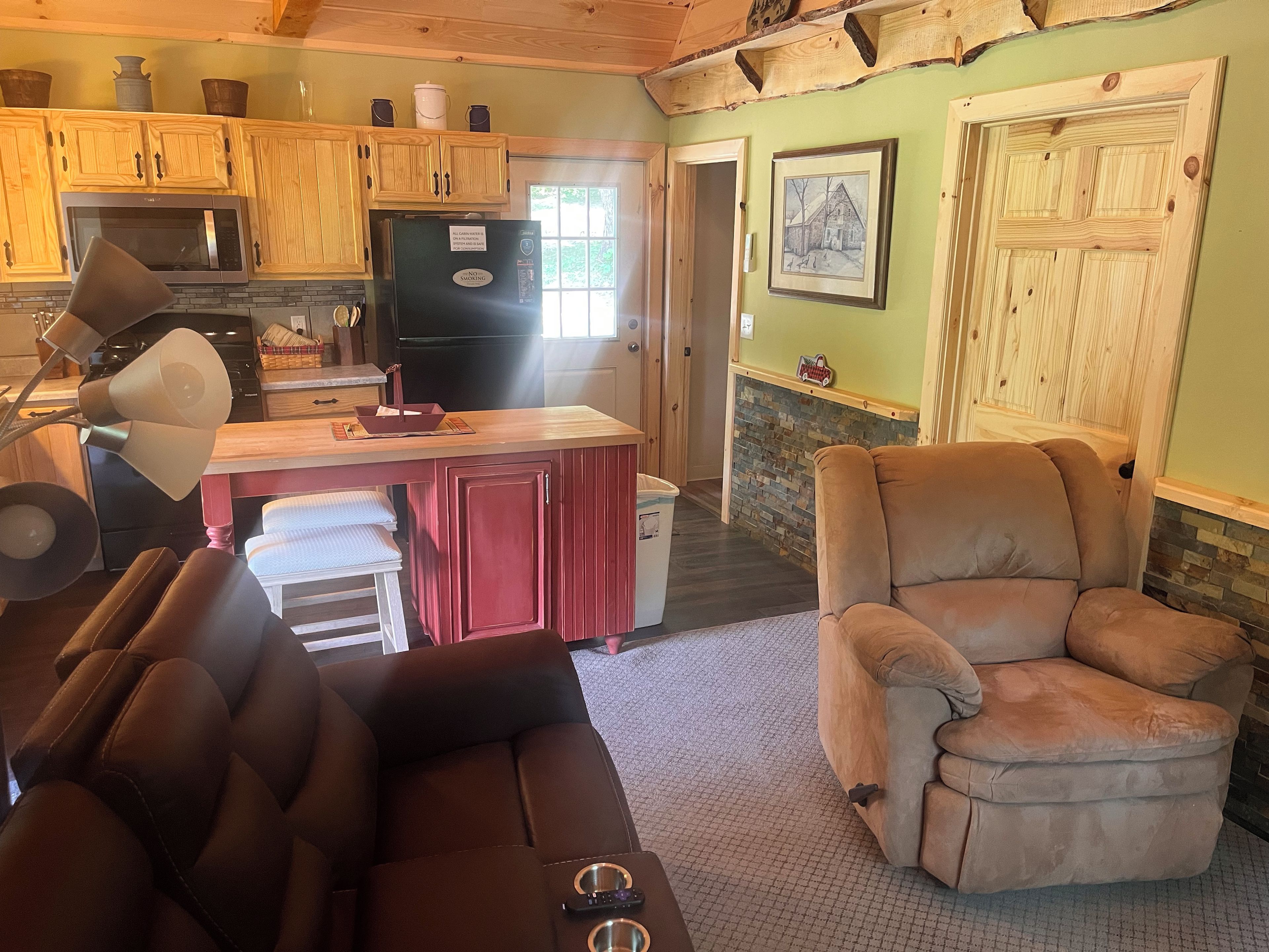 A cozy living room with a brown leather sofa, a recliner, and a kitchen area with wooden cabinets and a refrigerator.