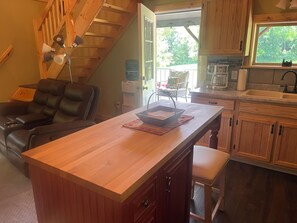 A kitchen with wooden cabinets, a countertop, and a window. - Floyd cabin (Dansville)