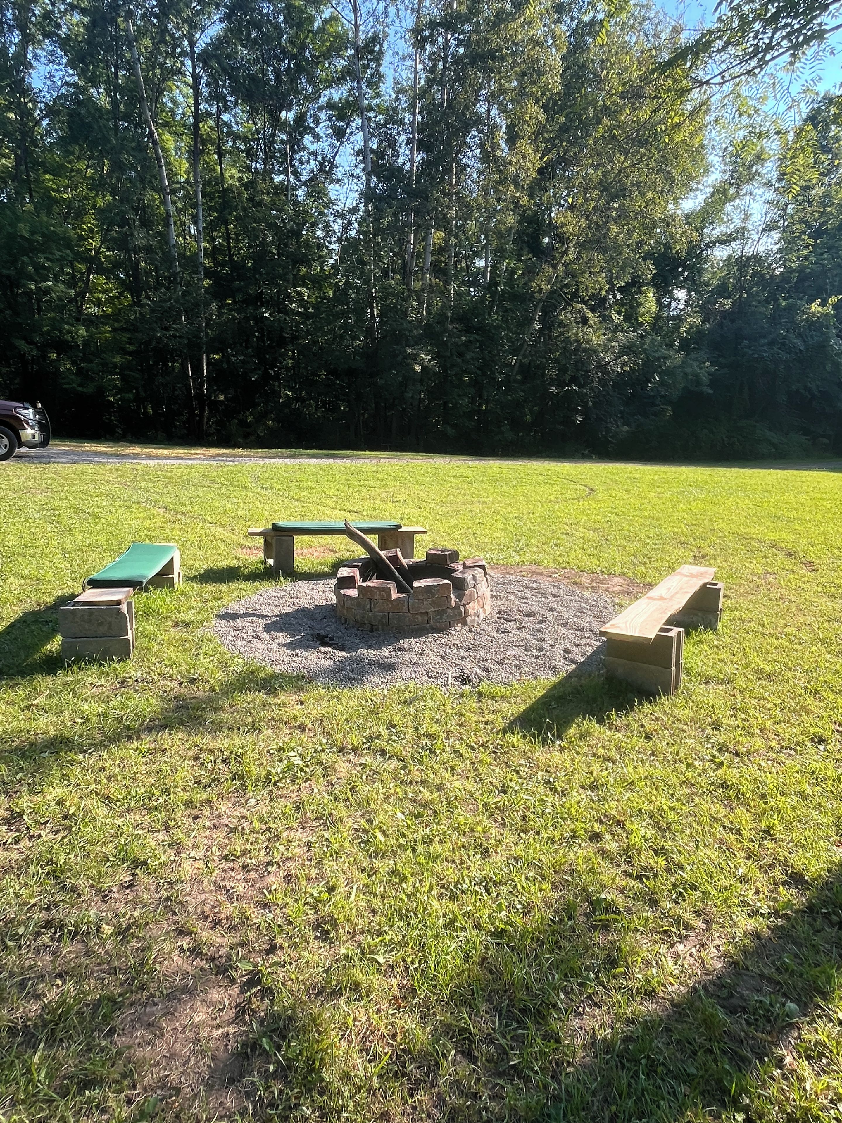 An outdoor seating area with benches and a fire pit surrounded by grass.