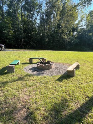 Ein Außenbereich mit Bänken und einem Feuerkorb, umgeben von Gras.