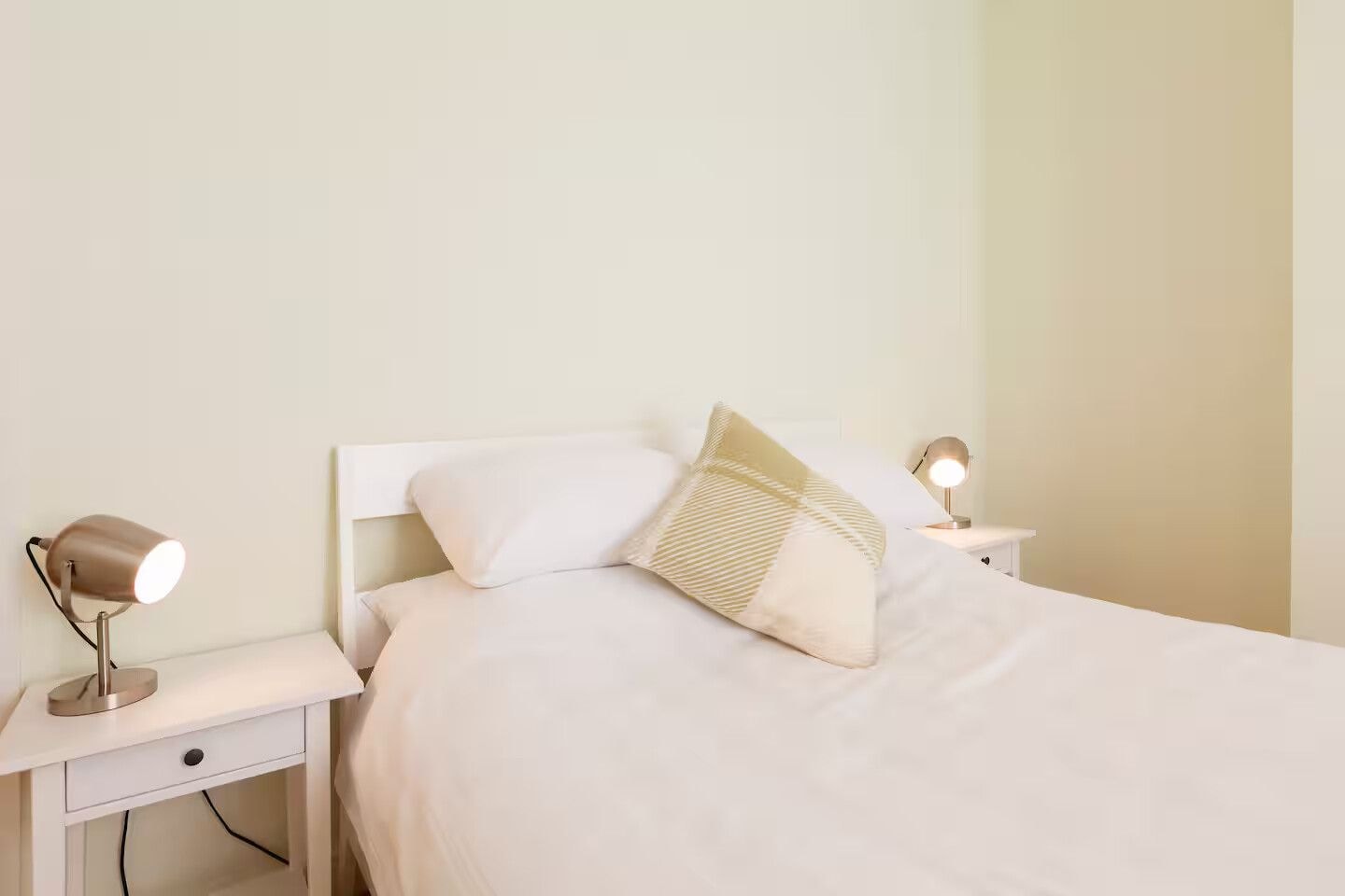 A neatly made bed with white bedding and two bedside lamps on white nightstands.