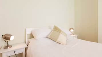 A neatly made bed with white bedding and two bedside lamps on white nightstands.