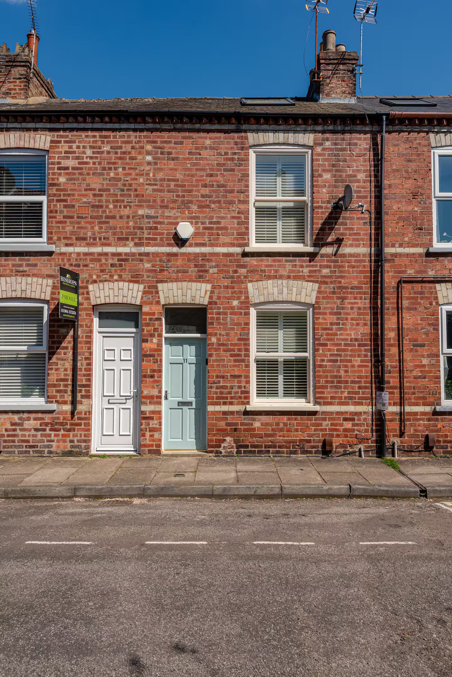 A red brick terraced house with a front door, two windows, and a chimney.