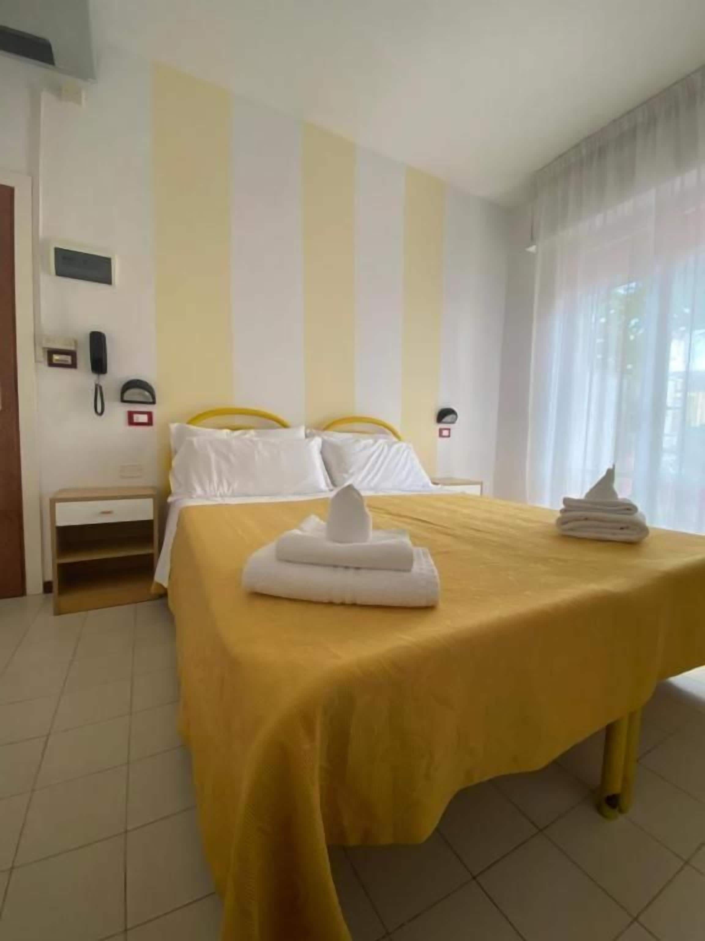 A hotel room with a bed, a bedside table, a telephone, and a window with curtains.