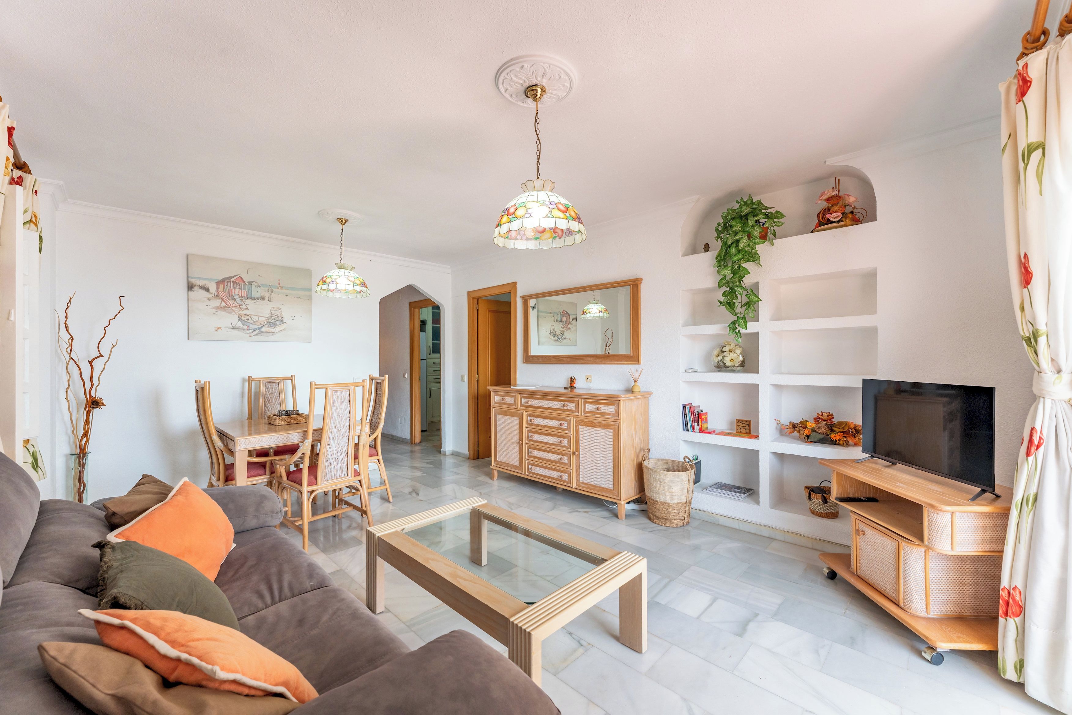 Ein Wohnzimmer mit Sofa, Couchtisch, Esstisch, Stühlen, Fernseher und Bücherregal.