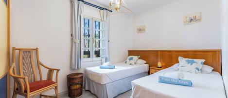 A hotel room with two single beds, a wooden chair, a wicker basket, and a window with curtains.