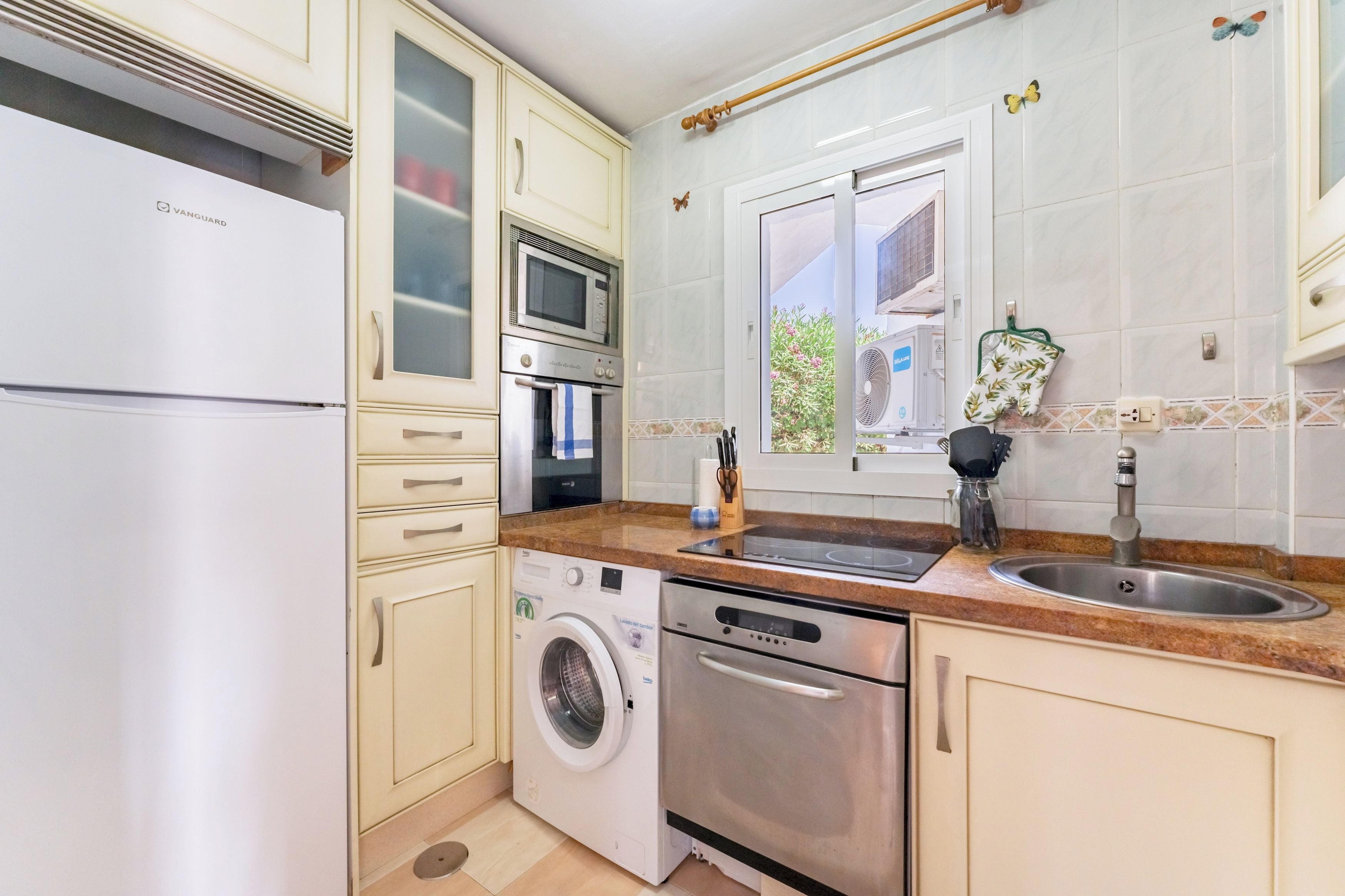 Eine kleine Küche mit Kühlschrank, Mikrowelle, Backofen, Waschmaschine und Spüle.