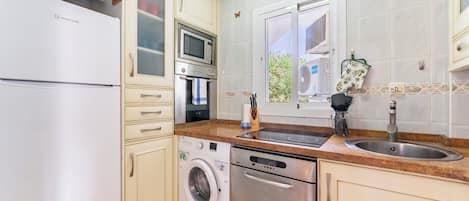A compact kitchen with a refrigerator, microwave, oven, washing machine, and a sink.