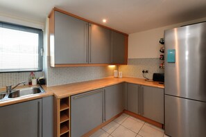 A modern kitchen with grey cabinets, a stainless steel refrigerator, and a tiled backsplash. - Marina-View Flat near Cardiff & Penarth - Pass the Keys (Penarth)