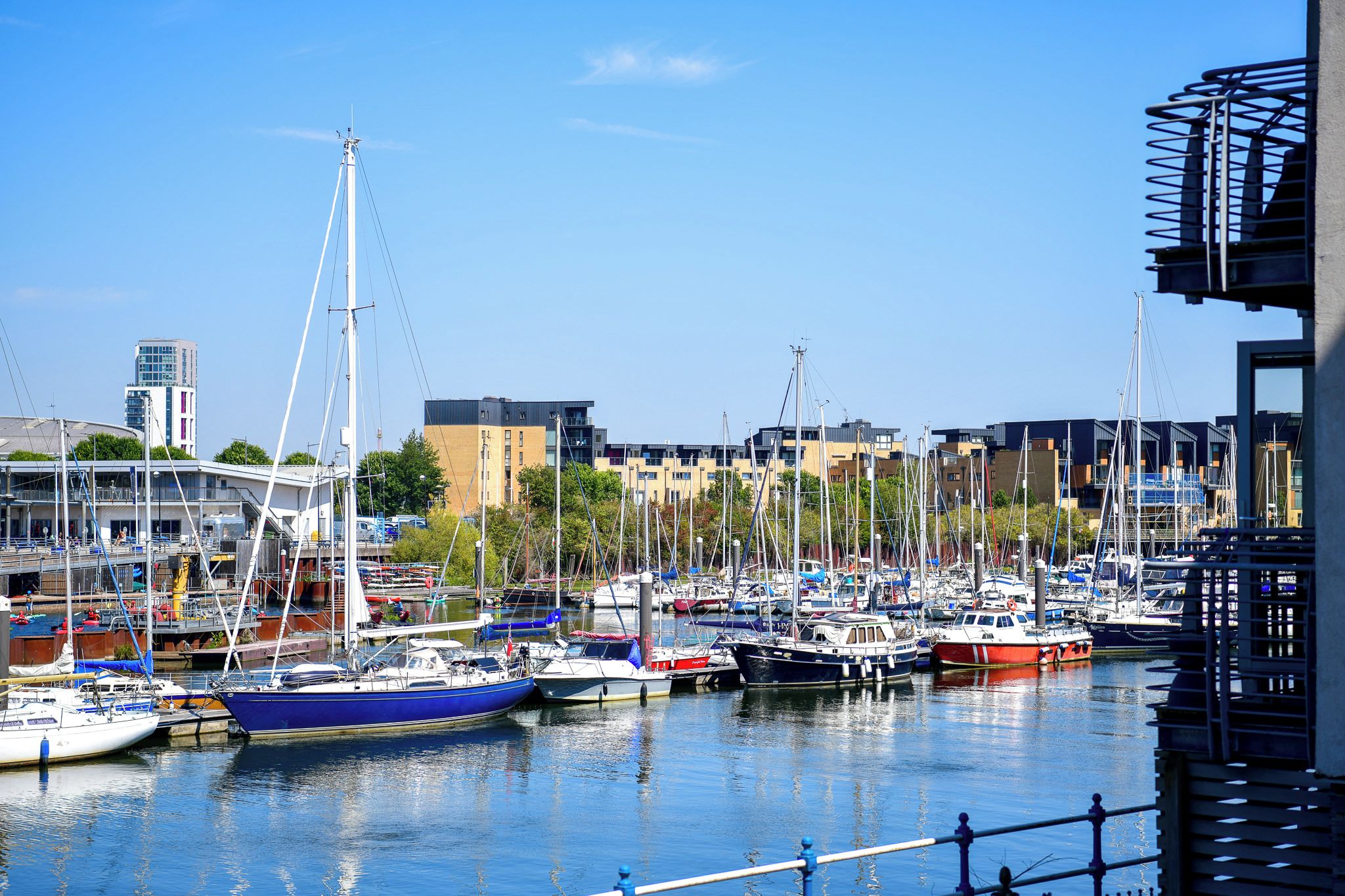 A marina with multiple boats docked, surrounded by modern buildings and a clear sky.