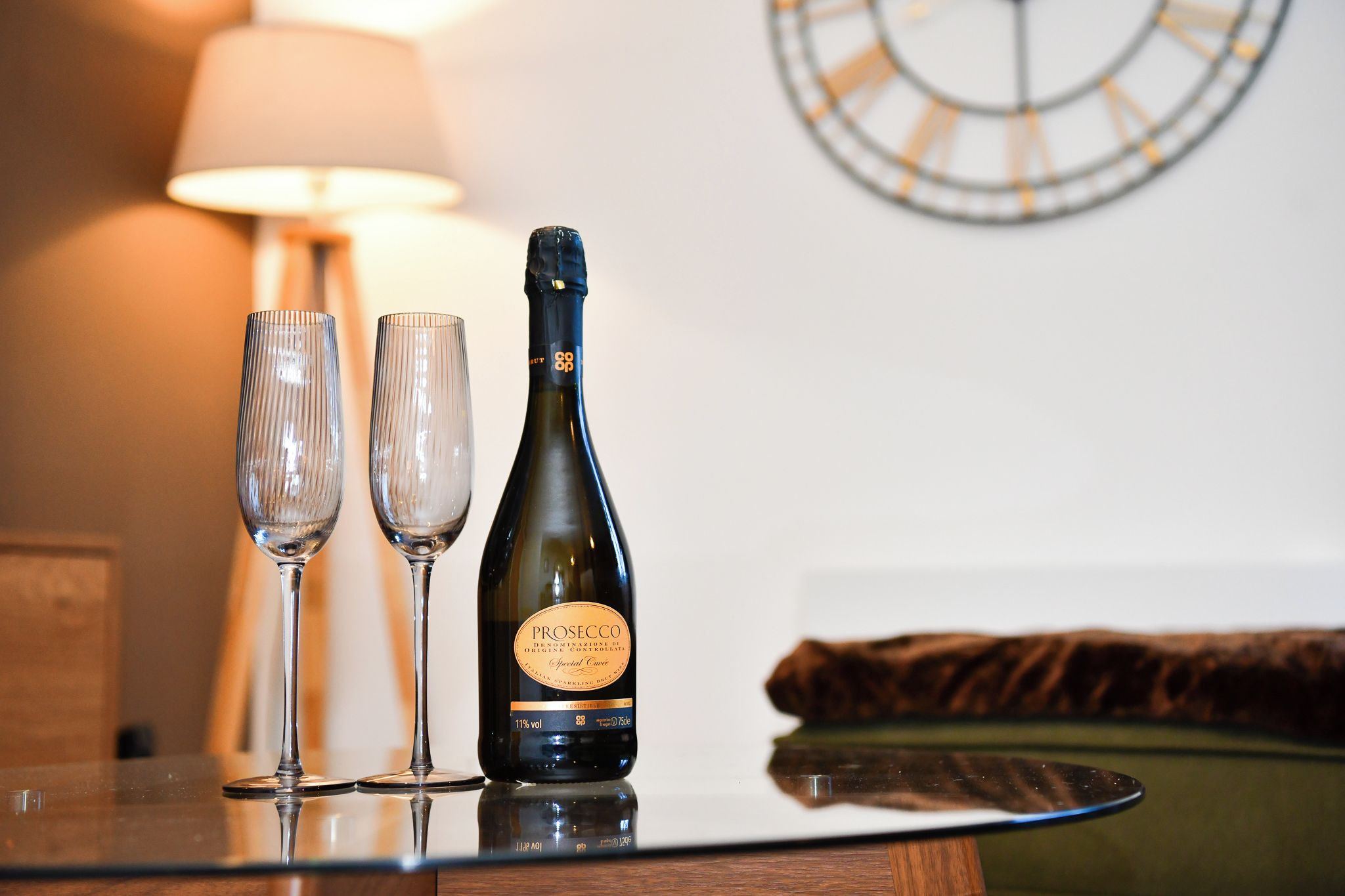 A bottle of Prosecco wine and two glasses on a reflective surface.