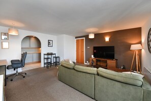 A modern living room with a sofa, a TV, a dining area with a table and chairs, and a kitchen visible through an archway. - Marina-View Flat near Cardiff & Penarth - Pass the Keys (Penarth)