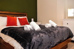 A neatly made bed with a black bedspread, two red pillows, and rolled white towels. - Marina-View Flat near Cardiff & Penarth - Pass the Keys (Penarth)
