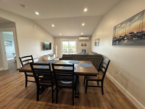 Un comedor con una mesa y sillas de madera, una cocina al fondo y un cuadro en la pared.