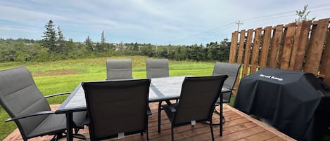 Ein Essbereich im Freien mit Tisch und Stühlen, einem Grill und Blick auf ein Wiesenfeld.