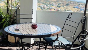 A patio with a round table and chairs, a view of a distant town, and a clear sky. - Maisonette with Rooftop Terrace at Bab Souk – AC, WiFi & Medina Views (Chefchaouen)