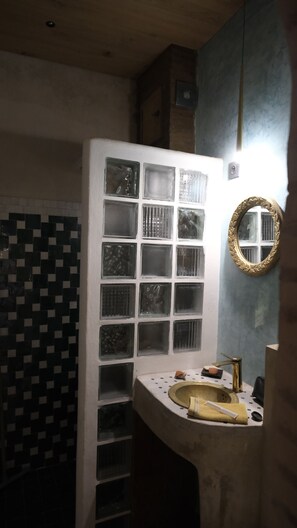Bany amb paret de rajola, un lavabo amb aixeta daurada i un mirall amb marc decoratiu.