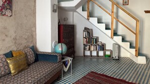A living room with a patterned sofa, a globe, a bookshelf, and a staircase. - Maisonette with Rooftop Terrace at Bab Souk – AC, WiFi & Medina Views (Chefchaouen)
