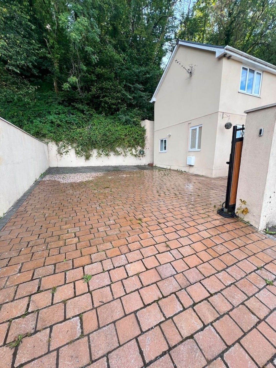 A paved patio area with a brick pattern, a white wall with a window, and a door.