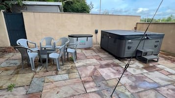 An outdoor patio with stone flooring, a hot tub, and a seating area with chairs and a table.