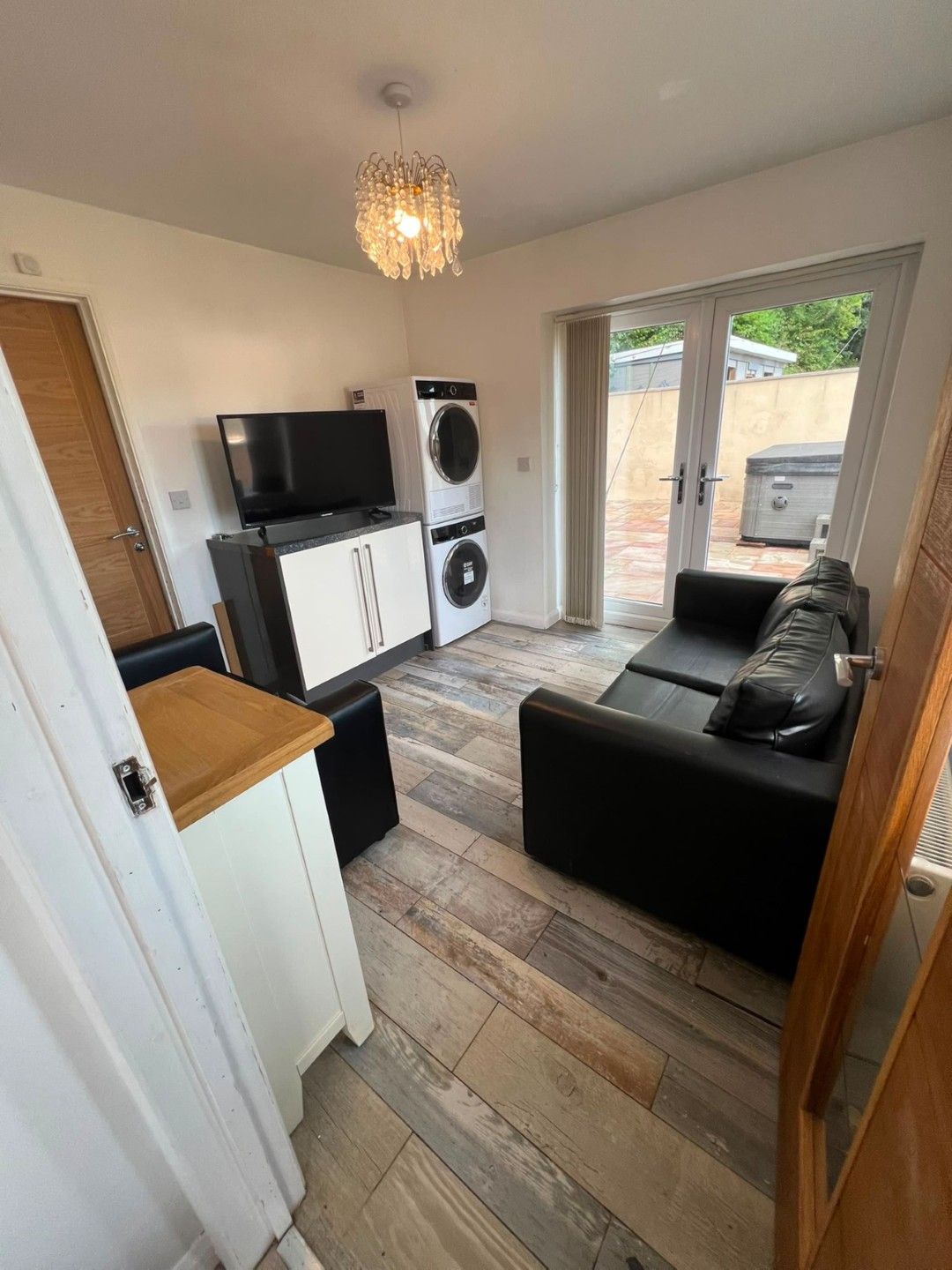 A compact living space with a kitchenette, a flat-screen TV, a washing machine, a sofa, and a dining area.