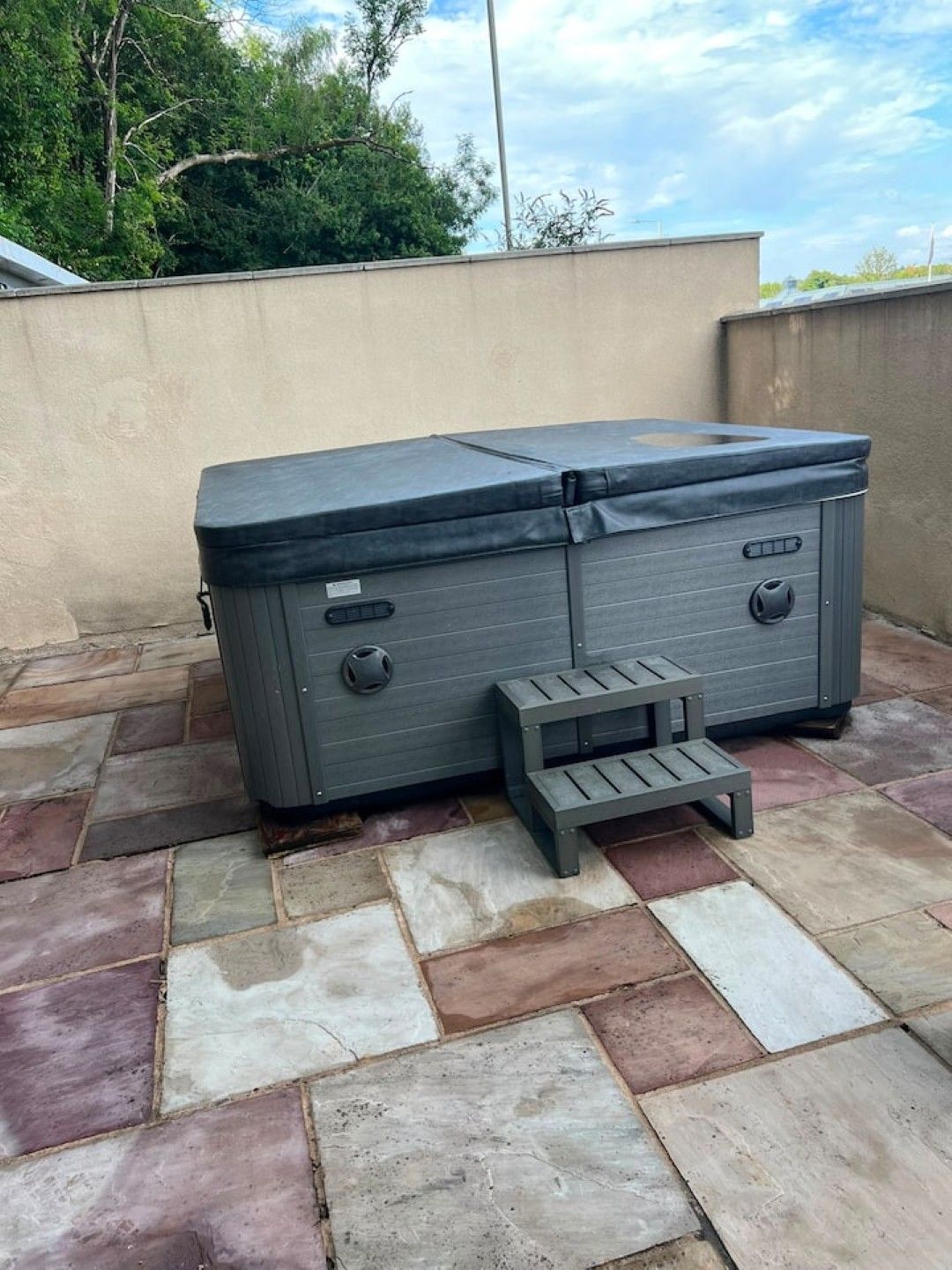A gray outdoor storage unit with a lid, a bench, and a step for access, placed on a stone patio.