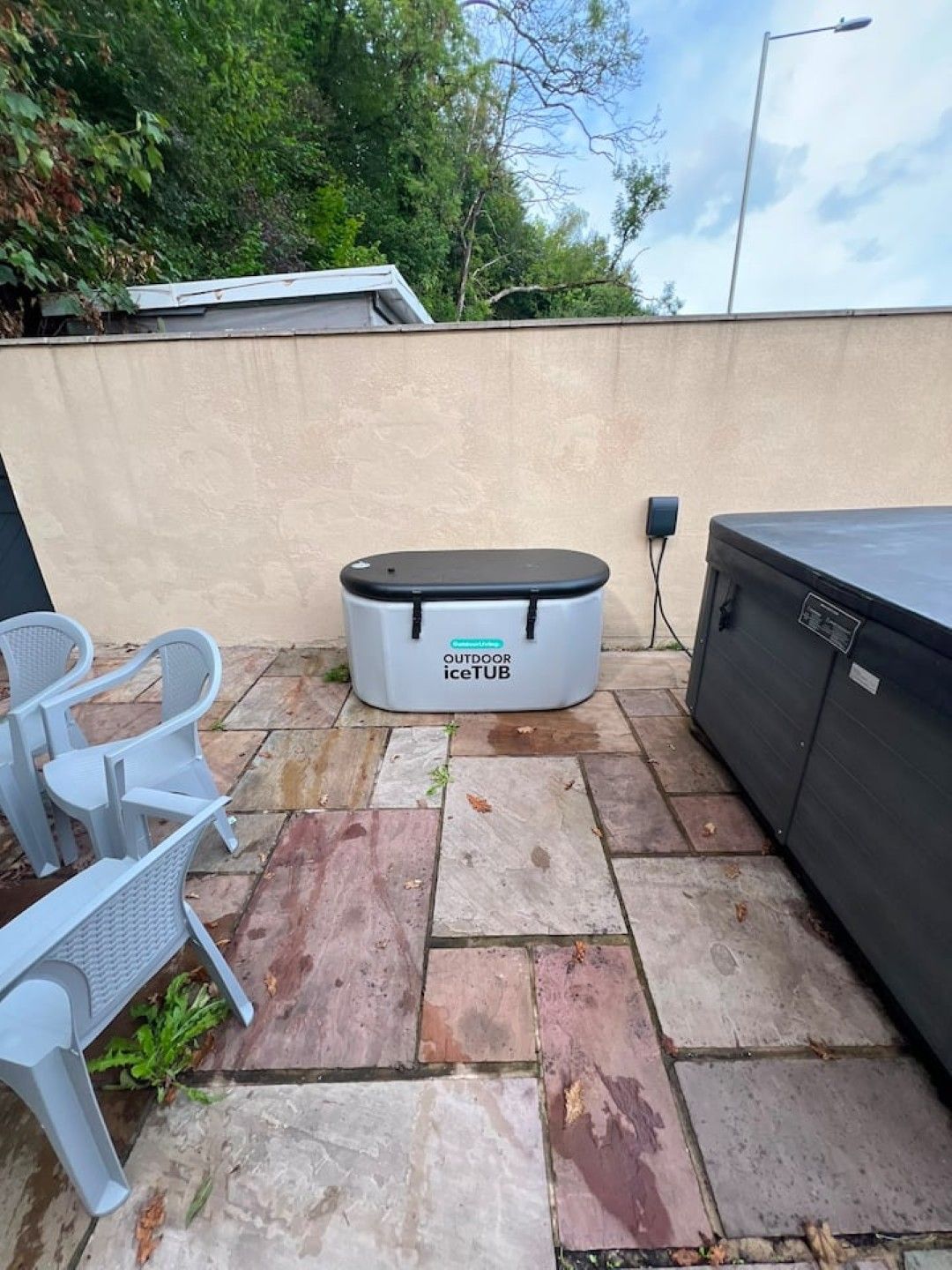 A patio area with stone flooring, a white outdoor iceTUB, and a seating arrangement with white chairs.