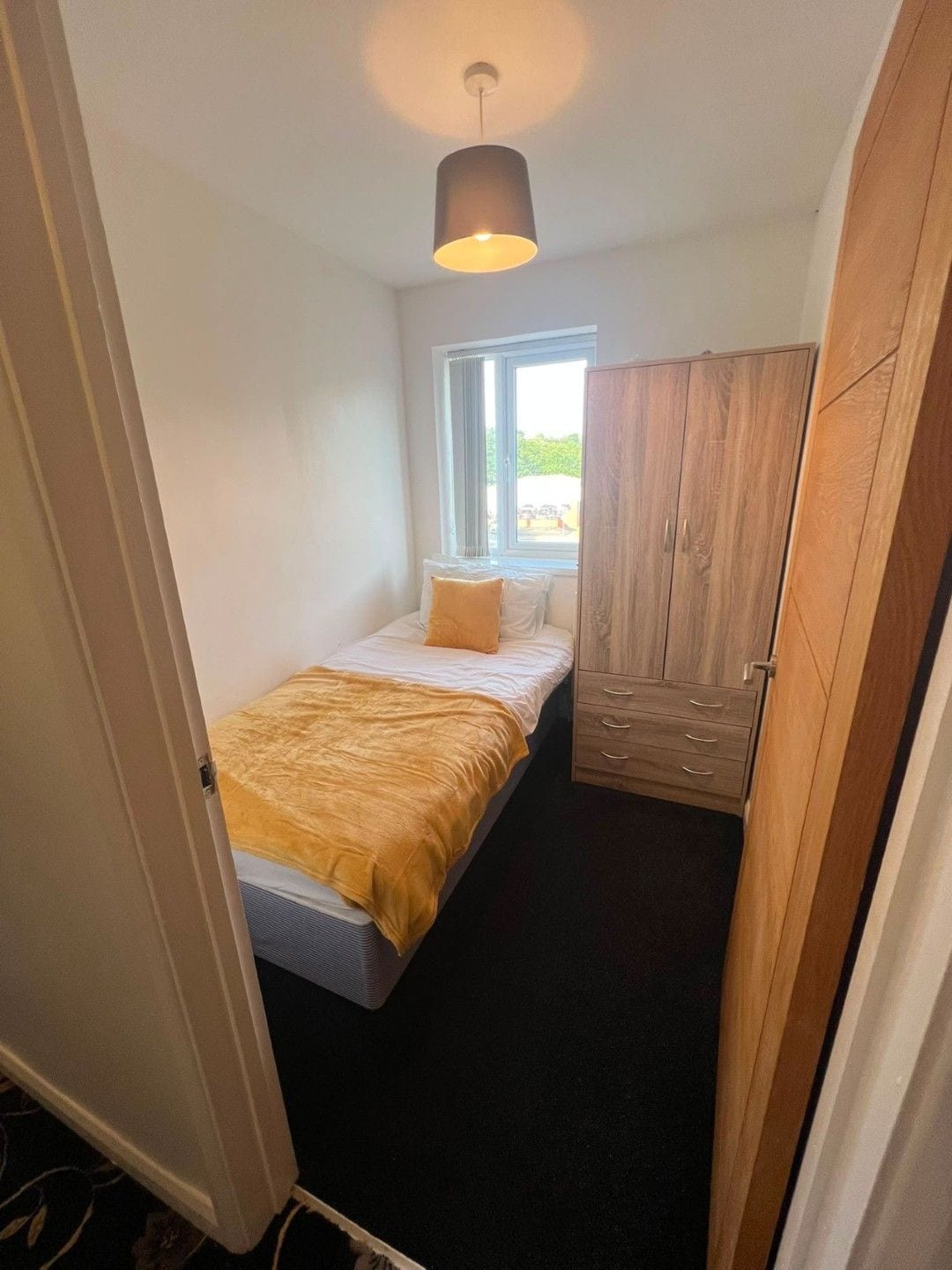 A narrow room with a bed, a window, and a wardrobe.