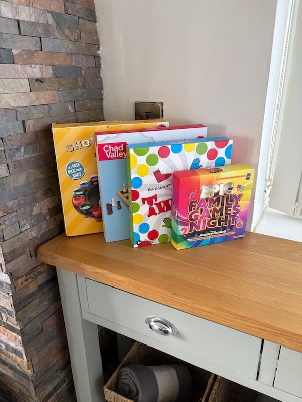 A wooden shelf with three board games: 'Chad Valley,' 'Fate Pick Your Shot,' and 'Fame Game Night.'