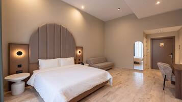 A modern hotel room with a large bed, bedside tables, a sofa, and a desk.
