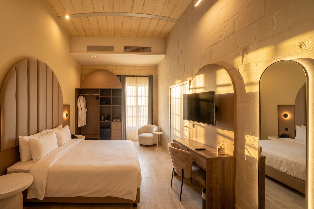 A modern hotel room with a large bed, a desk, a TV, and a walk-in closet.
