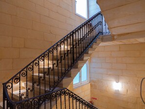 A staircase with ornate black railings and beige stone walls.