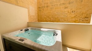 A hot tub with a control panel, set against a stone wall.