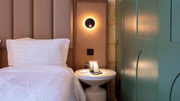A hotel room with a bed, a bedside table with a lamp, a telephone, and a wall-mounted light fixture.