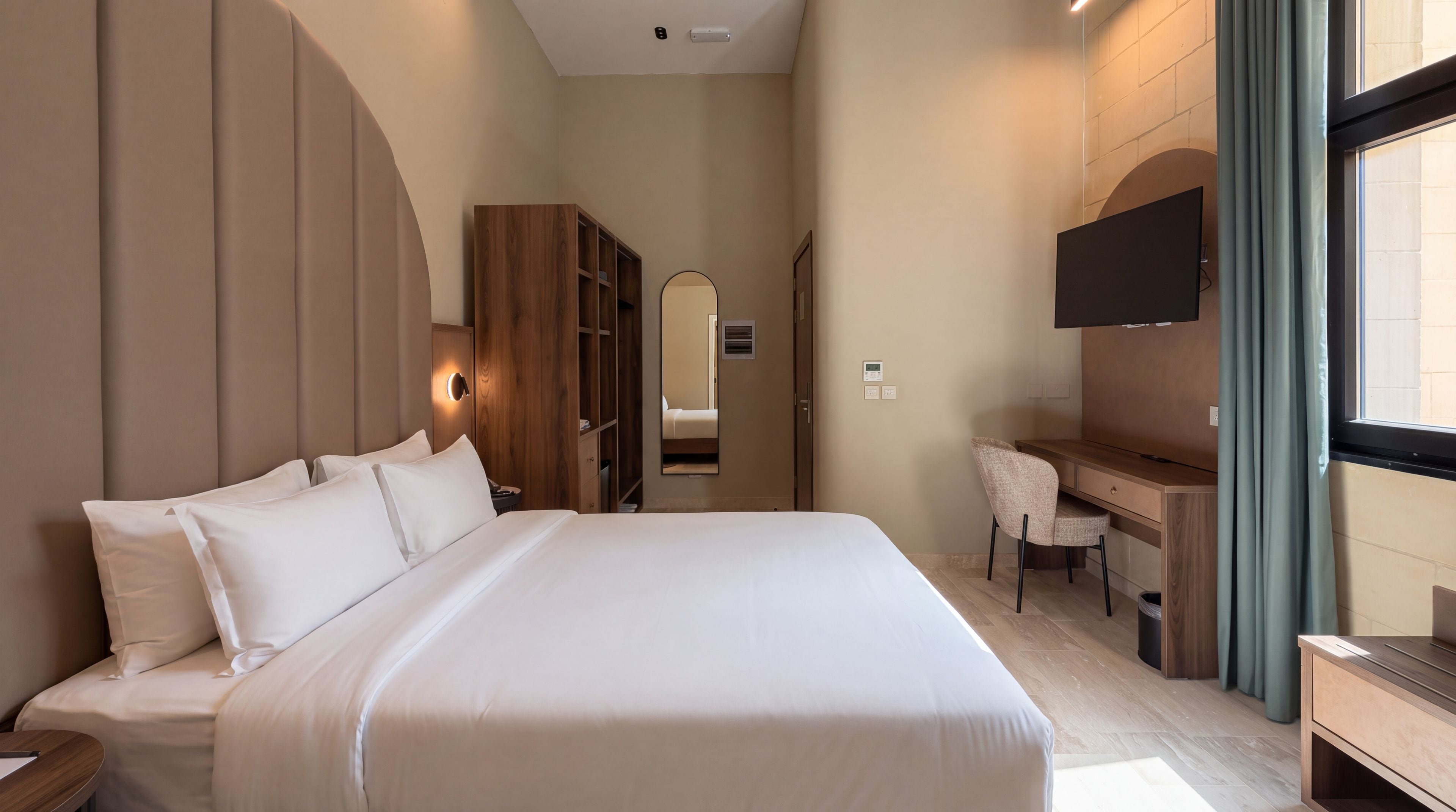 Ein Hotelzimmer mit einem großen Bett, einem Schreibtisch, einem Sessel, einem Fernseher und einem Kleiderschrank.