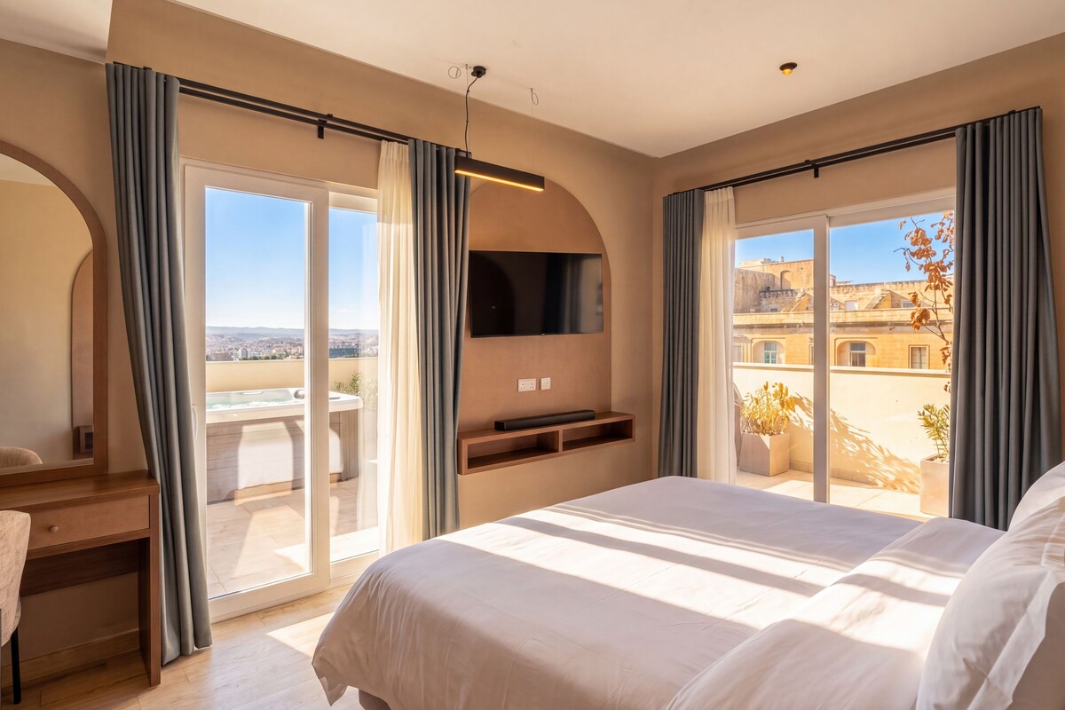 A hotel room with a large bed, a desk, a TV, and a balcony with a hot tub.