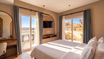 Quarto de hotel com uma cama grande, uma escrivaninha, uma televisão e uma varanda com banheira de hidromassagem.