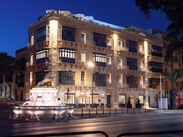 Un edificio de varios pisos con una fuente en primer plano, que cuenta con balcones y ventanas amplias.