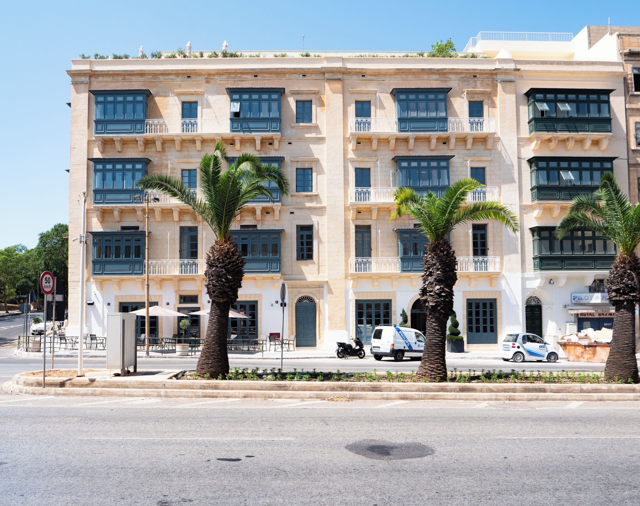 Un immeuble à plusieurs étages doté de balcons, de palmiers et de voitures garées.