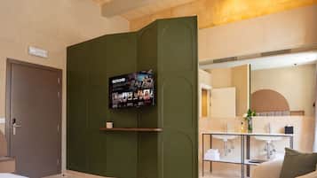 Une chambre d’hôtel moderne avec un grand lit, un téléviseur fixé sur un mur d’accent de couleur verte, une petite table avec un vase et une salle de bain équipée d’un lavabo et d’un miroir.