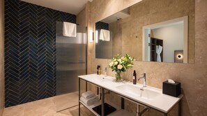 Casa de banho moderna com painel de azulejos em padrão herringbone, um espelho grande, uma pia branca e um vaso de flores.