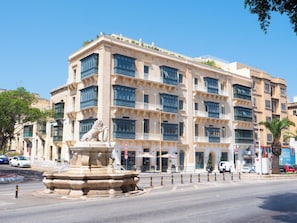 Un edificio de varios pisos con un patio central, una fuente con estatua de león y una calle con automóviles estacionados.