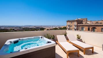 A rooftop terrace with a hot tub, lounge chairs, and a view of a cityscape.