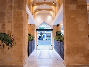 A hallway with stone walls, a glass door entrance, and potted plants. - St Anne Palace by Tritoni Prestige (Floriana)