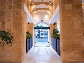 Un pasillo con paredes de piedra, un acceso por puerta de cristal y plantas en macetas.