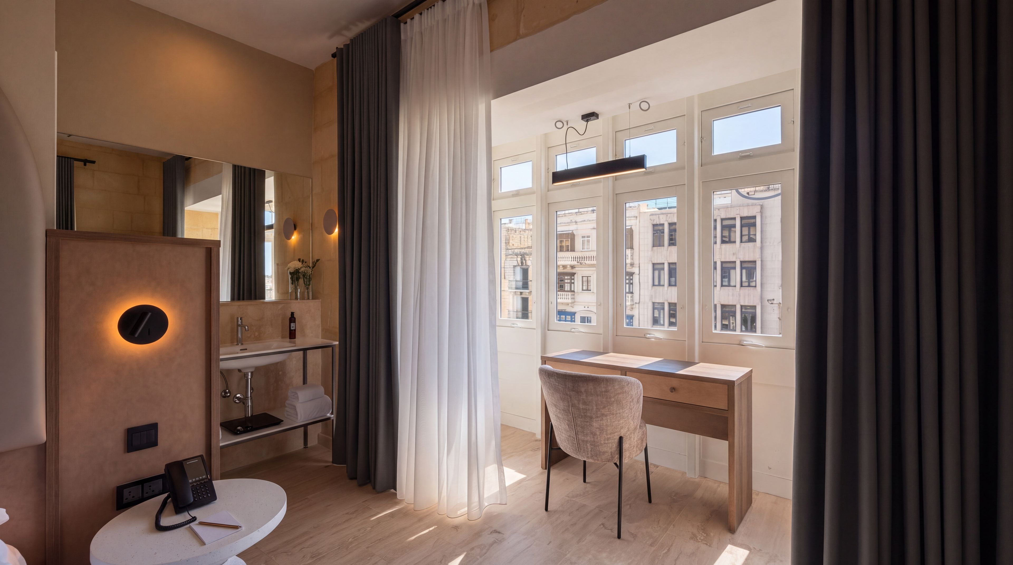 Ett modernt hotellrum med ett skrivbord, en stol och ett stort fönster med utsikt över staden.