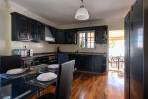 A modern kitchen with dark cabinetry, a dining table with chairs, a built-in oven, and a large window.