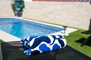Un área junto a la piscina con un bolso azul y blanco estampado sobre una silla.