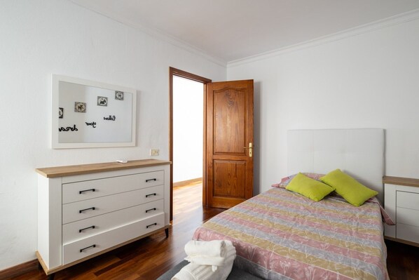 Un dormitorio con cama, cómoda, puerta y pared decorada con cuadros.