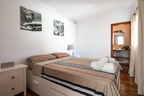 A hotel room with a bed, bedside tables, a nightstand, a lamp, a mirror, and a bathroom visible through an open door.